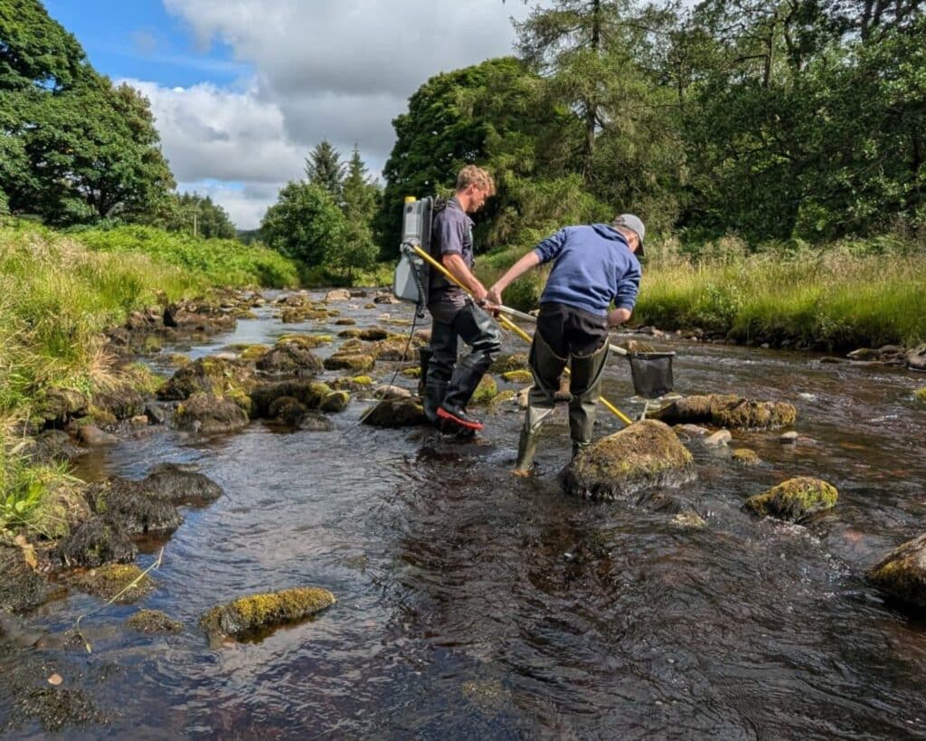 Two people wearing waders stand in the river examining the contents of fishing net.