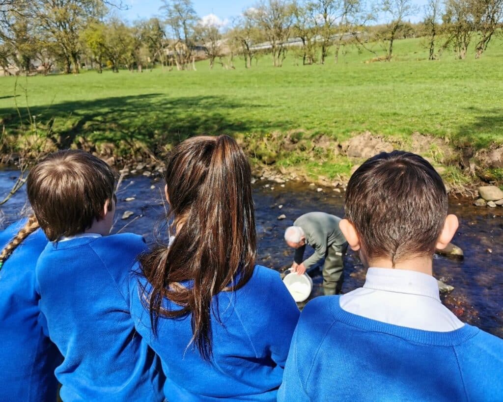 Pupils watch one of our education volunteers releasing trout- our amazing funders help us to deliver river workshops 
